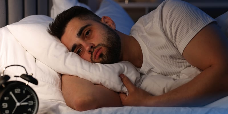 A man with ADHD laying down on his bed but unable to sleep