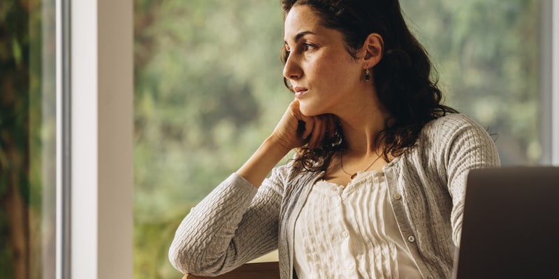 A lady sitting by the garden with hands on her chin thinking