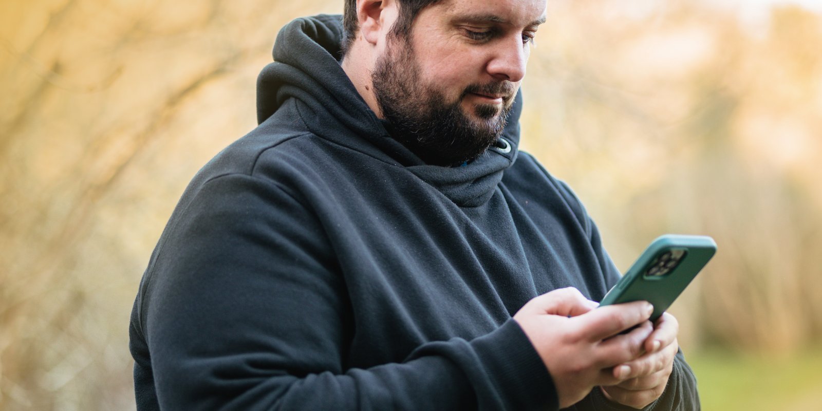 A man standing, holding his phone with two hands and looking into his phone