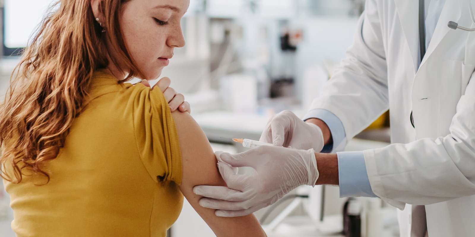 A girl wearing a year top with the sleeve rolled up receiving HPV vaccine from a nurse