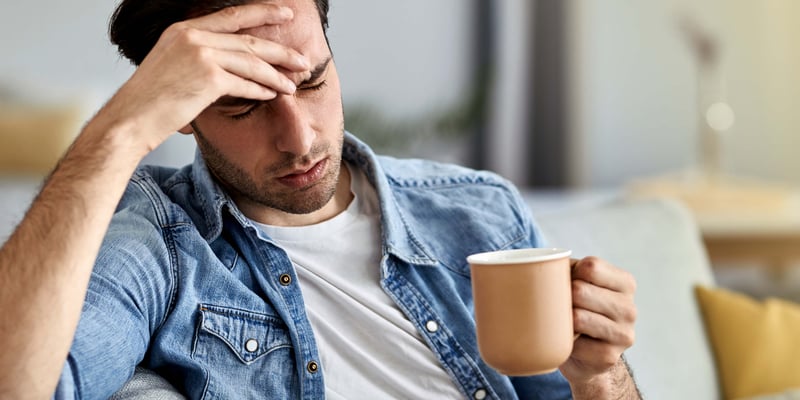 A man with a cup in hand and hand on his head feeling unwell