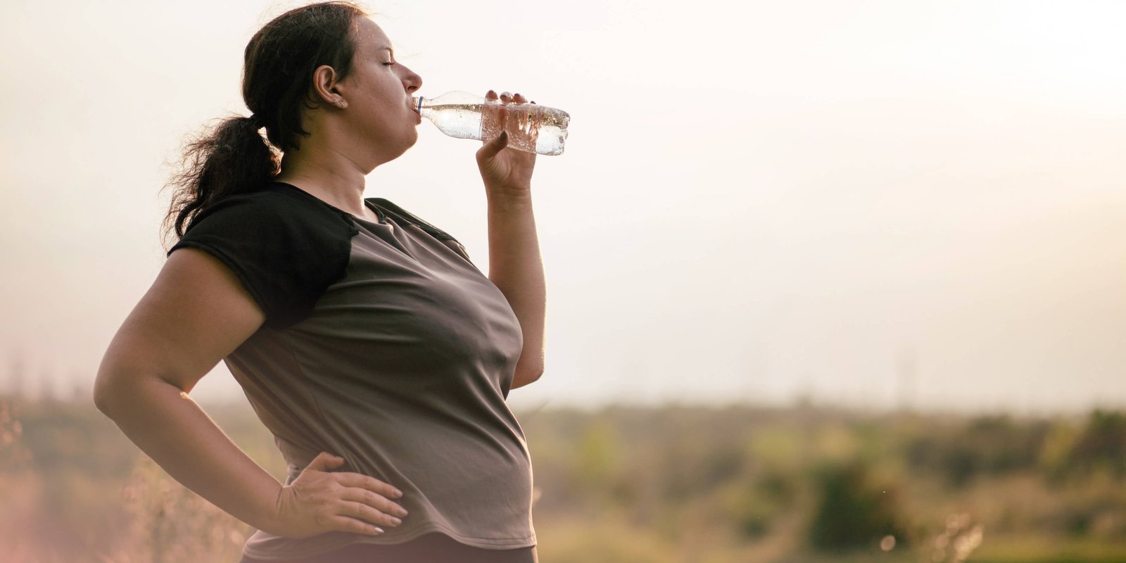 A fat woman walking on a path drinking water