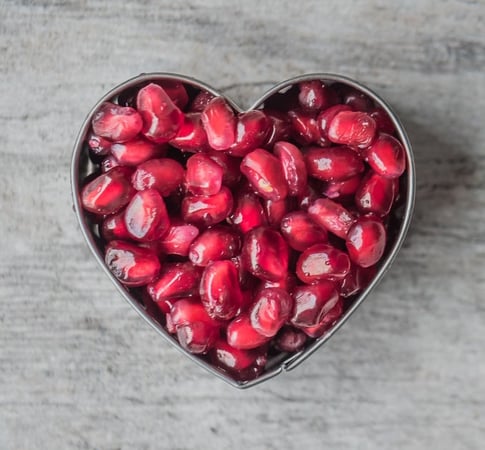 A heart shaped bowl filled with pomegranate 