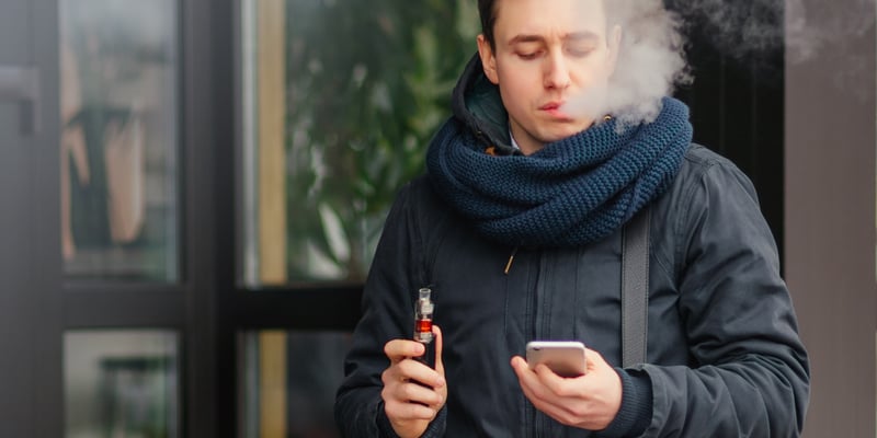 A man vaping outside while looking at his phone