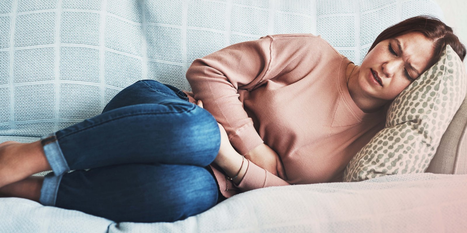 A woman laying on the couch holding her stomach in pains