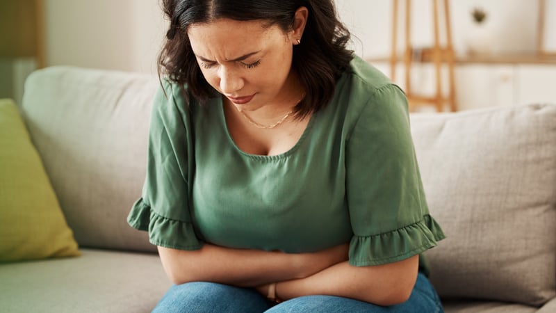 A woman sitting on a couch with hands holding her belly in pain