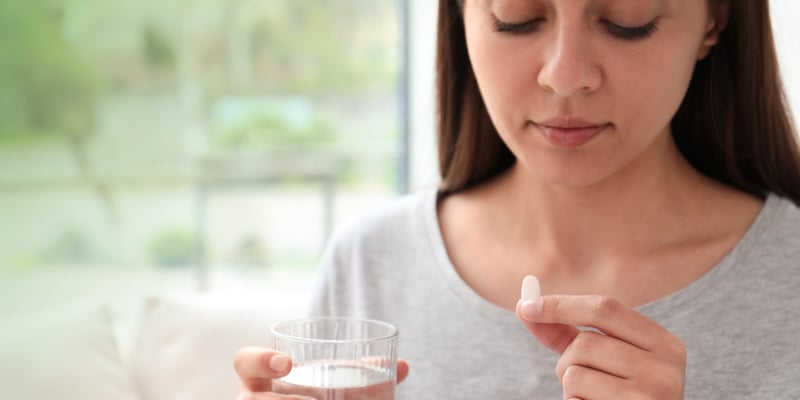 A woman holding a pill in one hand and a glass of water in another